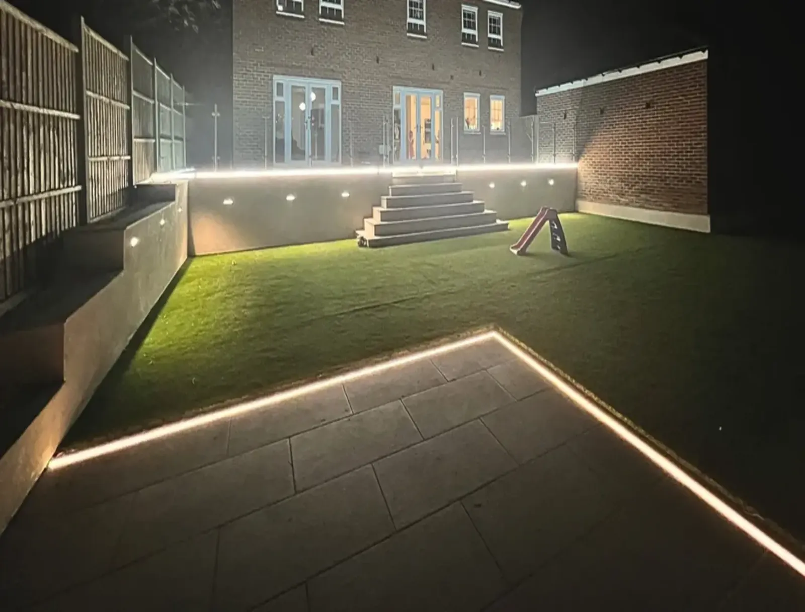 Warm LED strip lighting tracing a backyard patio edge and steps at night