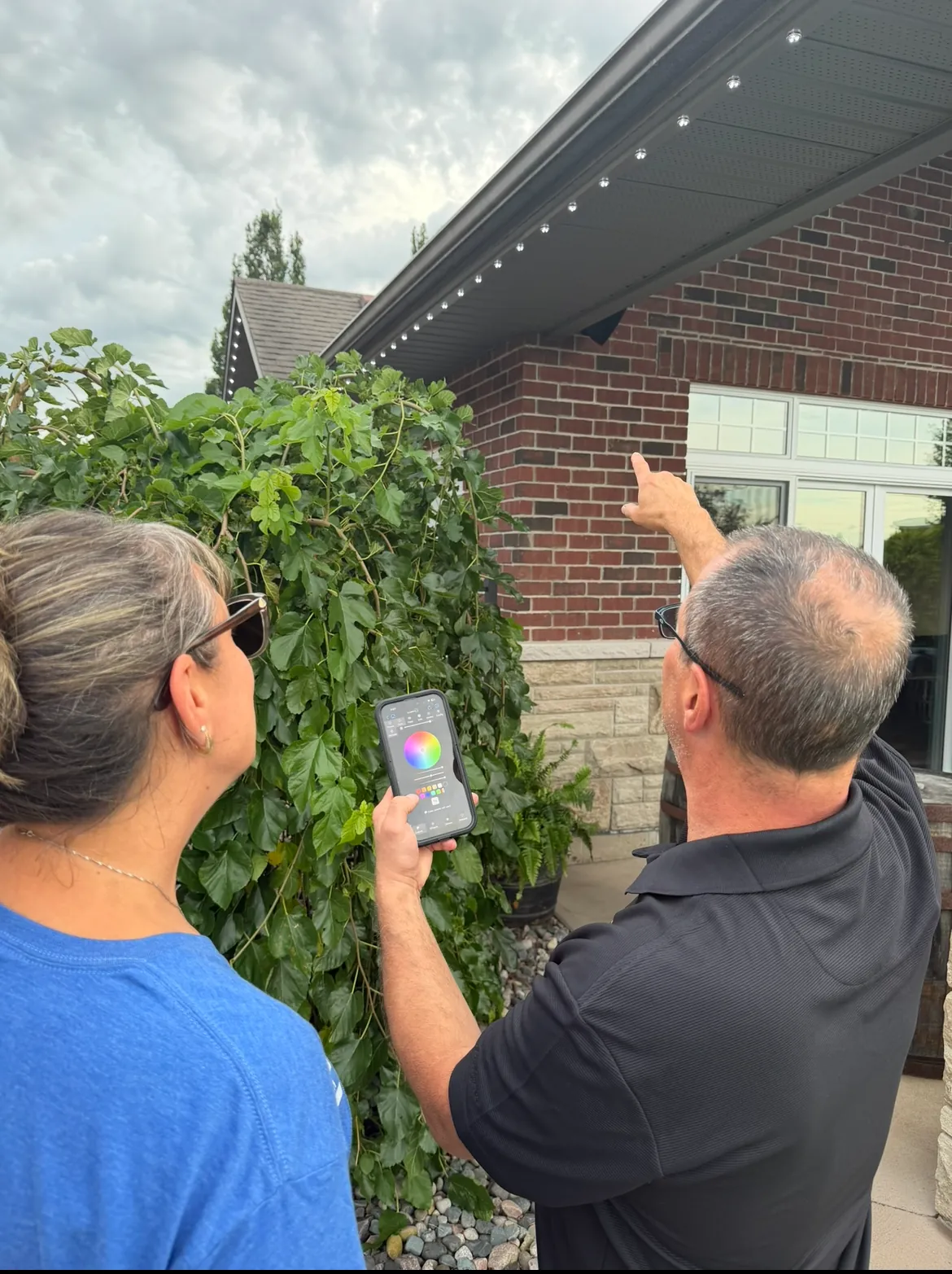 Installer showing a homeowner the lighting app beside newly installed soffit lights