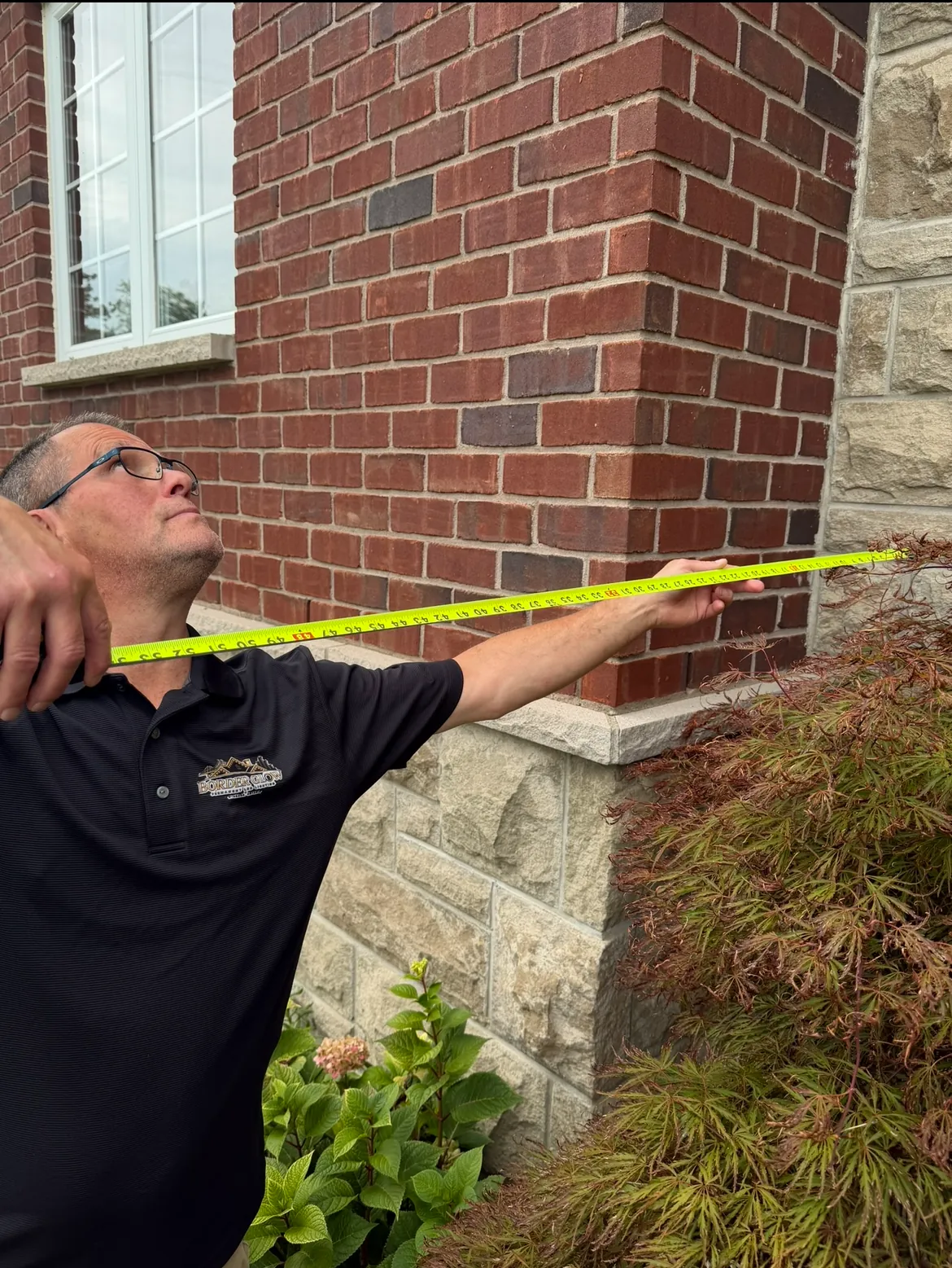 Technician measuring a brick home’s exterior with a tape measure before installation