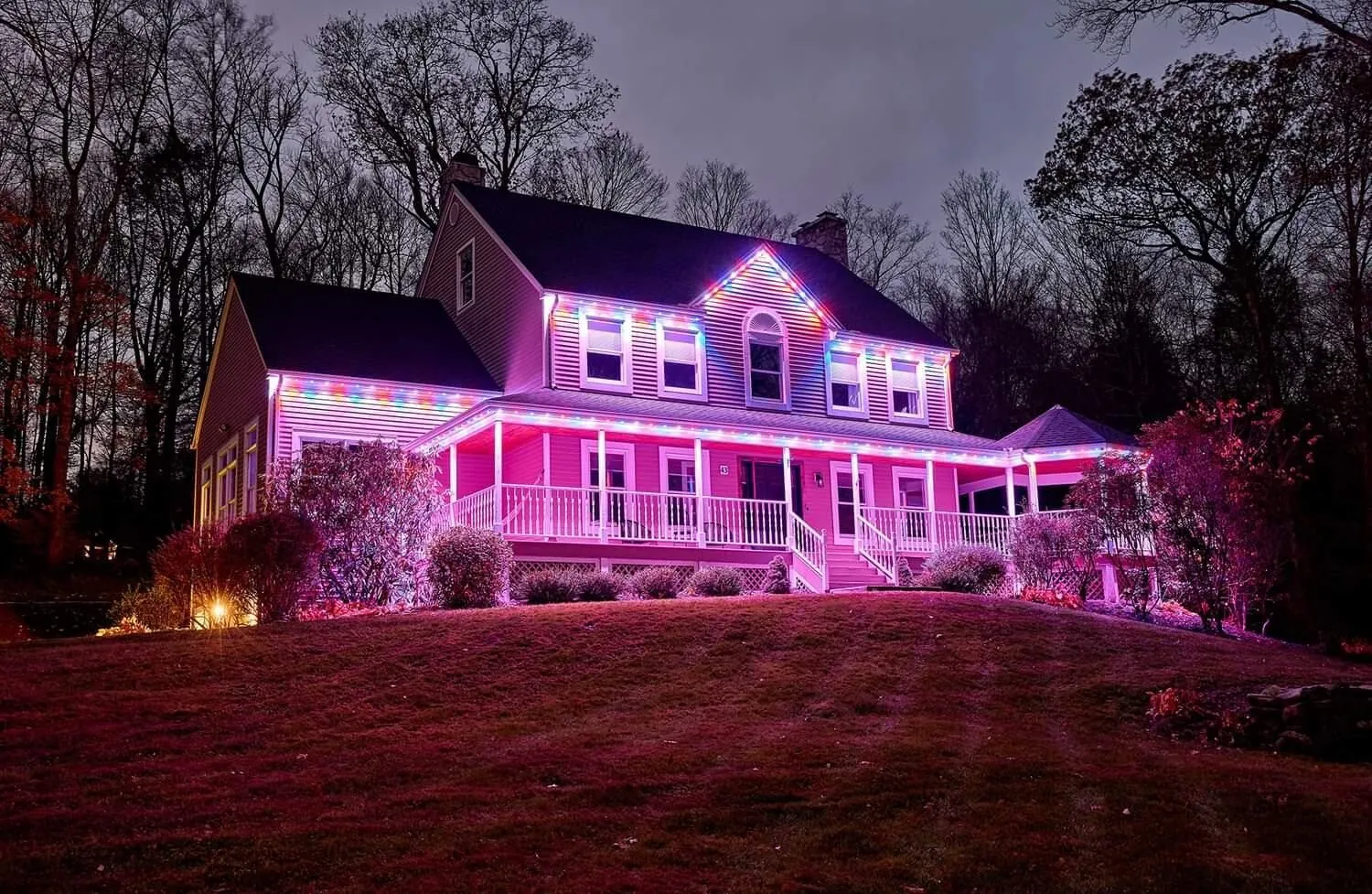Pink permanent lighting on a farmhouse-style home with a wraparound porch