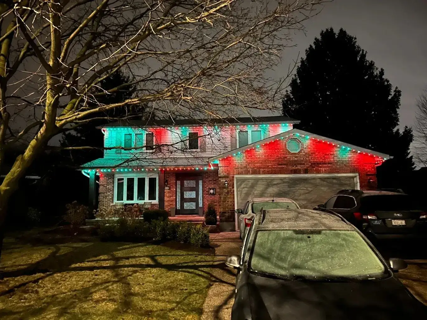Red and green holiday lighting on a two-storey brick home