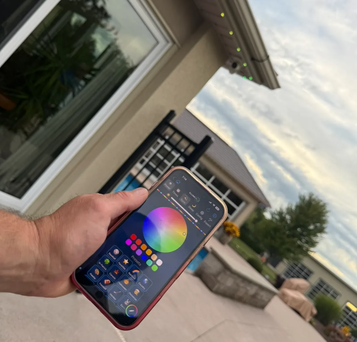 Hand holding a smartphone with a colour-wheel lighting app outside a home